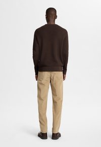 Suéter marrón de punto con un patrón texturizado, combinado con pantalones de pana beige y zapatos marrones. La vista muestra la parte trasera del conjunto.