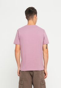 Lyslilla kortærmet T-shirt med rund hals, lavet af bomuld, blød tekstur, båret sammen med brune cargo-shorts, der viser en tatovering på armen.