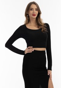Sort, langærmet crop top med rund udskæring, lavet af et strækbart materiale, parret med en matchende høj talje-nederdel med en slidse.
