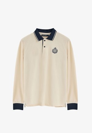 Langärmliges Poloshirt aus cremefarbenem Baumwollstoff mit navyfarbenem Kragen, drei Knöpfen und gesticktem Logo, das ein Kronen- und Lorbeerdesign zeigt.