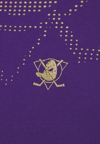 Tela morada con un tejido texturizado. Se presenta un logo dorado brillante de un pato con palos cruzados, rodeado de patrones de puntos dorados.