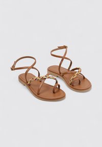 Sandalias de cuero marrón con tiras entrelazadas y detalle tejido multicolor. Suela plana y correas para el tobillo para un ajuste seguro.