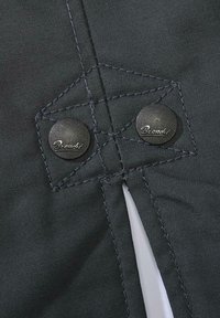 Czarna tkanina z widocznym przeszyciem, wyposażona w dwa metalowe zatrzaski z logo. Projekt zawiera wzmacniającą naszywkę w kształcie diamentu.