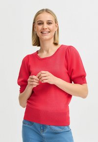 Pulover roșu tricotat cu mâneci scurte și puff, tiv texturat cu dungi și accente cu nasturi pe mâneci. Purtați cu blugi albaștri.