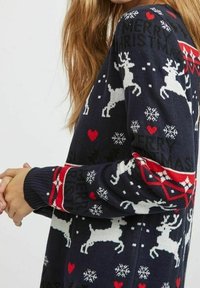 Pull marin avec des rennes blancs et des cœurs rouges, orné de flocons de neige et du texte "JOYEUX NOËL" dans un motif festif sur un tissu en maille douce.