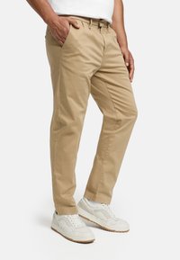 Chinos kaki en coton, présentant une coupe droite, des poches latérales et une texture lisse, assortis à des baskets blanches.