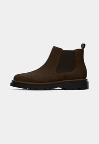 Botine Chelsea din suede maro, cu panouri elastice pe laterale, vârf rotunjit și o talpă groasă din cauciuc negru cu model pentru aderență.
