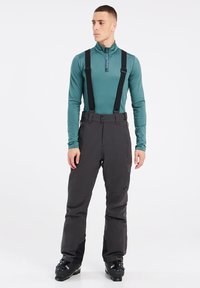 Mannen ski-outfit bestaande uit een teal langemouwen shirt en zwarte geïsoleerde broek met verstelbare bretels. Duurzame materialen, gestroomlijnd ontwerp.