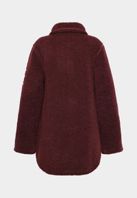 Bordeaux-värinen fleece-takki, jossa on teksturoitu pinta, leveä kaulus ja väljä leikkaus. Pehmeä materiaali, pitkät hihat ja pyöristetty helma.