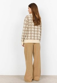 Beige houndstooth-mustriga kampsun ribadega varrukates, koos laiade khaki pükste ja. Pehme soonik tekstuur ja lõdva istumisega.