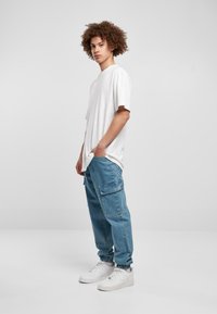Hvid t-shirt med korte ærmer, blå cargo-bukser med sidelommer og hvide sneakers. Casual, afslappet pasform; glat tekstur og lyse farver.