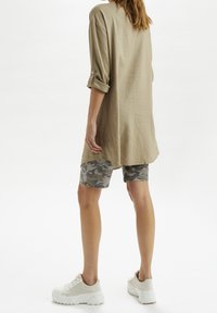 Khaki tuniek met opgerolde mouwen, gecombineerd met grijze camouflage shorts en witte sneakers; van zachte stof met een ontspannen pasvorm.