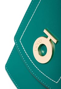 Tealfarbene Handtasche aus Kunstleder mit einem goldenen, runden Logo und weißen Nähten. Das Design verfügt über einen Klappenverschluss in geometrischer Form.