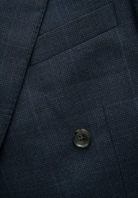 Tessuto di blazer blu navy con una leggera trama a reticolo, caratterizzato da un bottone tondo scuro davanti e un dettaglio di tasca discreto.