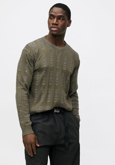 Ελιές πράσινο πουλόβερ πλεχτό με κατακόρυφες υφασμάτινες ρίγες και λογότυπο 'Iceberg', συνδυασμένο με μαύρο παντελόνι με κορδόνι. Απλός σχεδιασμός με λαιμόκοψη.