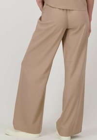 Beige wijde broek met een gladde textuur en een ontspannen pasvorm, met een middelhoge taille en een zoom die net boven de schoenen valt.