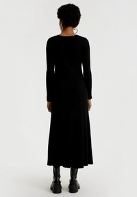Schwarzes geripptes Maxikleid mit langen Ärmeln, einem Rundhalsausschnitt und einem fließenden Schnitt, kombiniert mit klobigen schwarzen Plateaustiefeln.