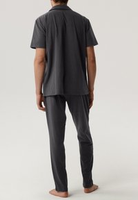 Szara koszula z krótkim rękawem i pasujące do niej spodnie z miękkiego materiału. Koszula ma klasyczny kołnierzyk; spodnie są proste, lekkie i proste w formie.