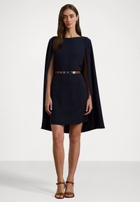 Navy blue dress with cape sleeves, fitted waist, and a metallic belt. Smooth fabric, knee-length design, and open back detail.