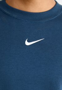Námořnická modrá mikina z bavlny, se bílým vyšívaným logem Nike na hrudi a s designem žebrovaného výstřihu.