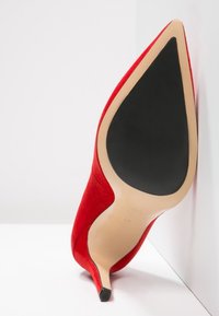 Scarpa con tacco a stiletto in suede rosso, con punta affusolata e suola in gomma nera, caratterizzata da una texture liscia e un design minimalista.