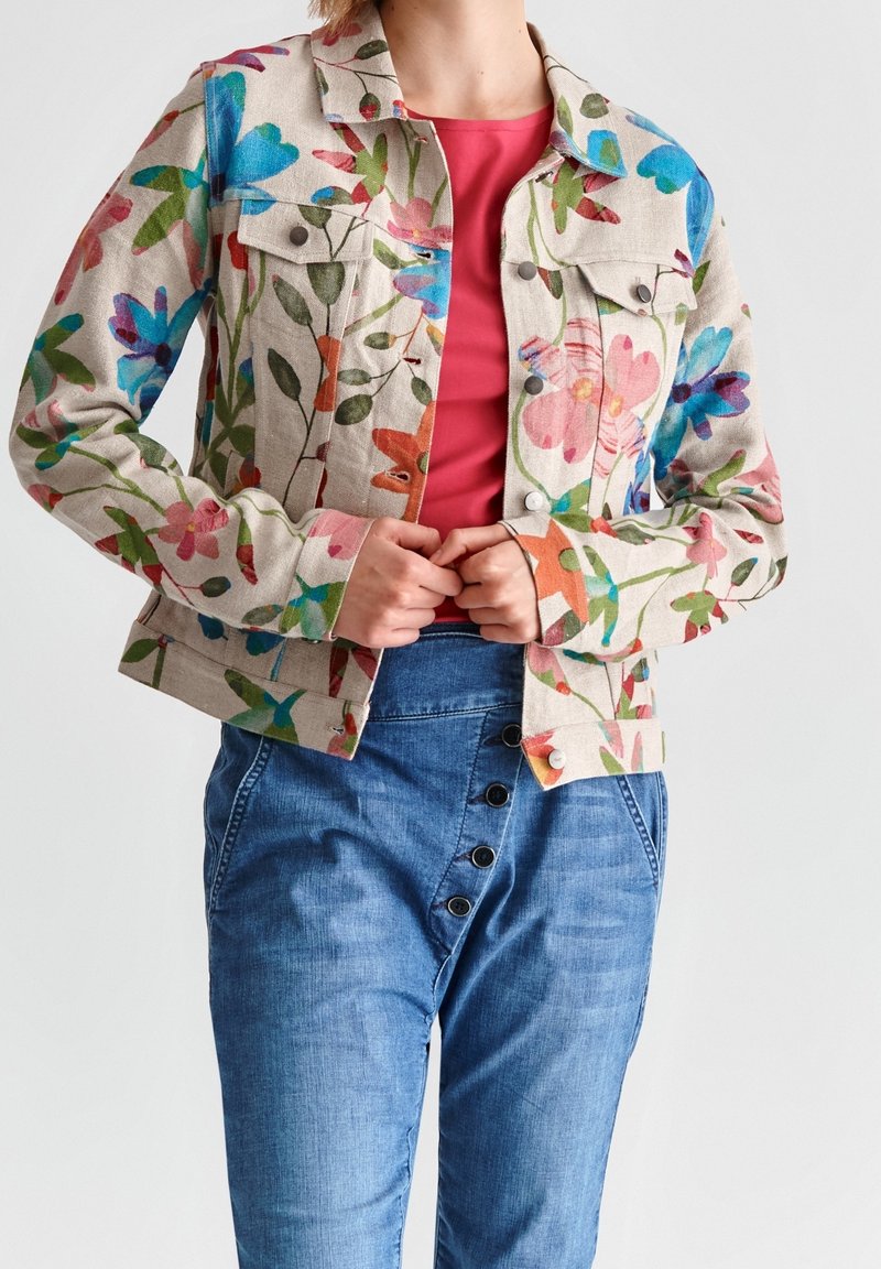 Beige denim jack met bloempatronen; heeft een kraag, een knoopsluiting en zakken; gecombineerd met blauwe tapered broeken.