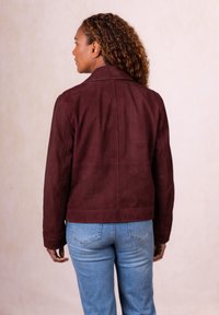Burgundy suede jacket with a structured collar, fitted design, and long sleeves, paired with light blue denim jeans.