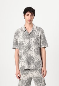 Camicia a maniche corte con bottoni in grigio chiaro e bianco, con un motivo botanico testurizzato; presenta un colletto e bottoni neri.