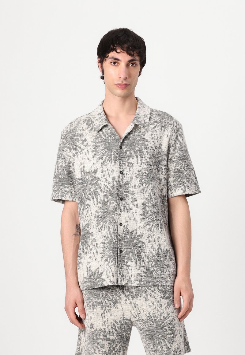 Camicia a maniche corte con bottoni in grigio chiaro e bianco, con un motivo botanico testurizzato; presenta un colletto e bottoni neri.