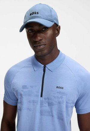 Homme portant une casquette BOSS bleu clair et un polo zippé assorti avec un motif subtil sur la poitrine, sur fond uni.