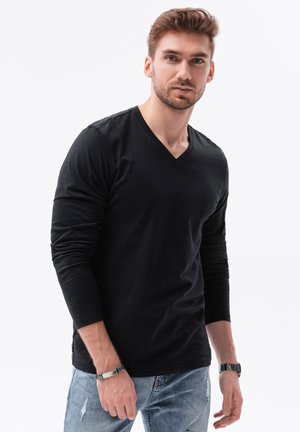 Camiseta negra de manga larga con escote en V, hecha de algodón, con un diseño ajustado y una ligera textura. Combinada con jeans azules desgastados.