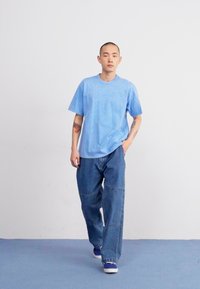 Μπλε βαμβακερό μπλουζάκι με κοντά μανίκια, σε συνδυασμό με χαλαρούς μπλε τζιν παντελόνες και ναυτικές αθλητικές πατούσες. Απλός σχεδιασμός, ελάχιστες λεπτομέρειες.