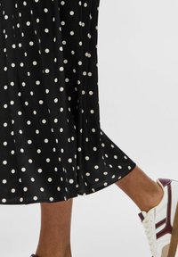 Mustaline seelik valgete täppidega, millel on voldid ja voolav disain, koos burgundiaaktsentidega valgete tennisekingadega.