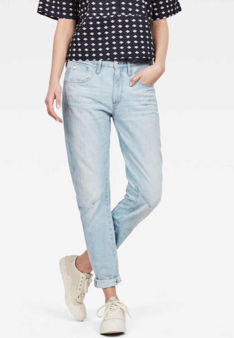 Ljust blå denim jeans med avslappnad passform, upprullade vid vrister. I kombination med en mörk mönstrad topp och ljusa sneakers.