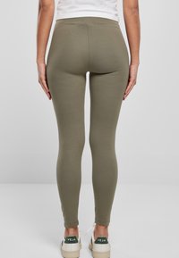 Olijfgroene leggings van rekbare stof, met een hoge tailleband en een slim fit, gecombineerd met witte sneakers met groene accenten.