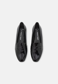 Czarne lakierowane mokasyny wykonane ze skóry, z zaokrąglonym noskiem i ozdobnym paskiem na cholewce. Wnętrze prezentuje markę i rozmiar.