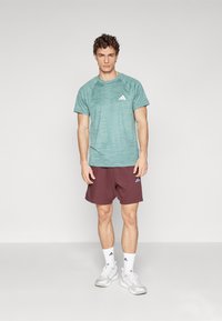 Light teal athletic t-shirt with short sleeves and a textured pattern, paired with maroon shorts featuring white logo accents. White sneakers included.
