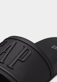 Sandale noire à enfiler avec une large bride arborant le logo "GAP" en relief, dotée d'une semelle intérieure texturée et d'un design minimaliste.