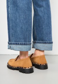 Bruine suède instappers met een zwarte en luipaardprint zool, gecombineerd met cropped blauwe denim jeans met opgerolde zomen.