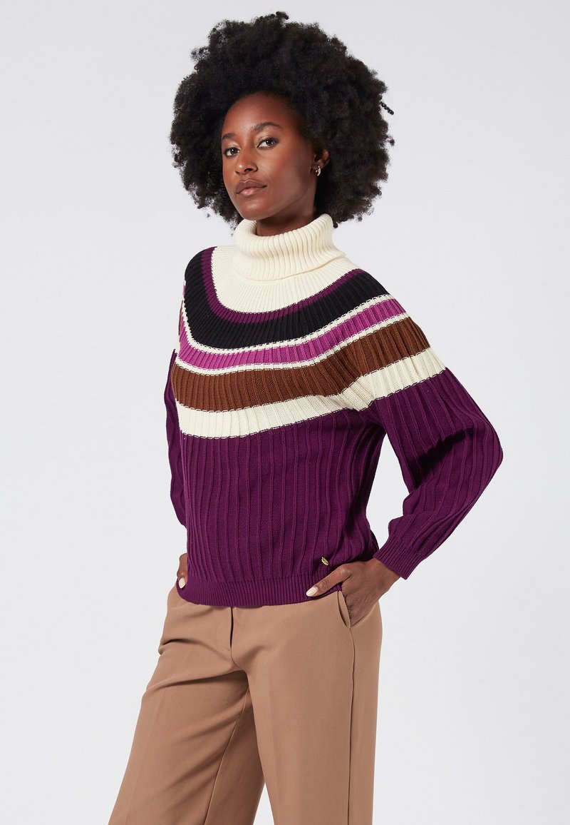 Stickad polotröja med horisontella ränder i kräm, burgund, brunt och svart. Ribbad textur med en lila kropp.