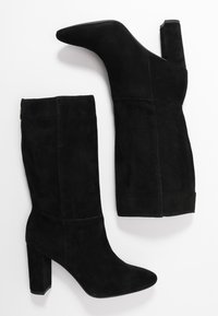 Černé semišové kotníkové boty s vysokým blokovým podpatkem, špičatou špičkou a hladkým povrchem. Charakterizují se bezešvým designem bez viditelného kování.
