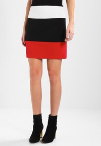 Falda corta y ajustada con bloques de color horizontales: negro, blanco y rojo. Tejido suave; sin patrones visibles. Combinada con botas negras hasta el tobillo.