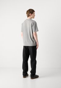 Gray cotton t-shirt with short sleeves, paired with loose-fitting black denim pants and dark shoes, shown from the back.