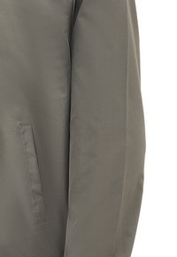 Veste grise avec une finition lisse et mate. Dispose d'une poche latérale sans matériel visible, mettant en valeur un design épuré.