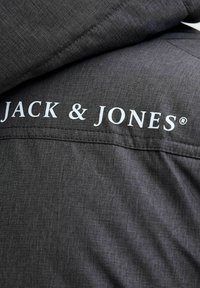 Grå hættejakke med struktureret stof. Har hvidt "JACK & JONES" logo på den øverste del af ryggen. Enkel design, skræddersyet pasform.