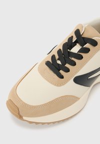 Sneakers beige et crème avec des lacets noirs, en cuir lisse et avec une texture en daim, bout rond et semelle en caoutchouc avec un motif structuré.