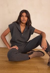 Gray knit jumpsuit with a zippered collar, short sleeves, and tapered legs. Features a smooth texture and a relaxed fit. Worn with brown ankle boots.