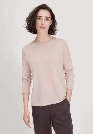 Helles rosa Strickoberteil mit lockerer Passform und Bootsausschnitt, langärmlig und mit leicht gewelltem Saum, kombiniert mit dunklen Hosen.