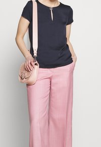 Marinblå kortärmad topp med nyckelhålsringning, kombinerad med rosa vida byxor och en liten rosa lädercrossbodyväska med kedjedetaljer.