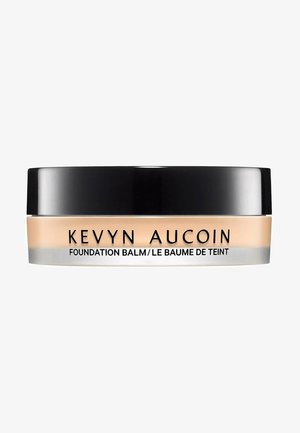 Kevyn Aucoin Foundation Balm in a clear jar with a black lid. The balm has a beige tint and a smooth surface. Silver detailing on the base.